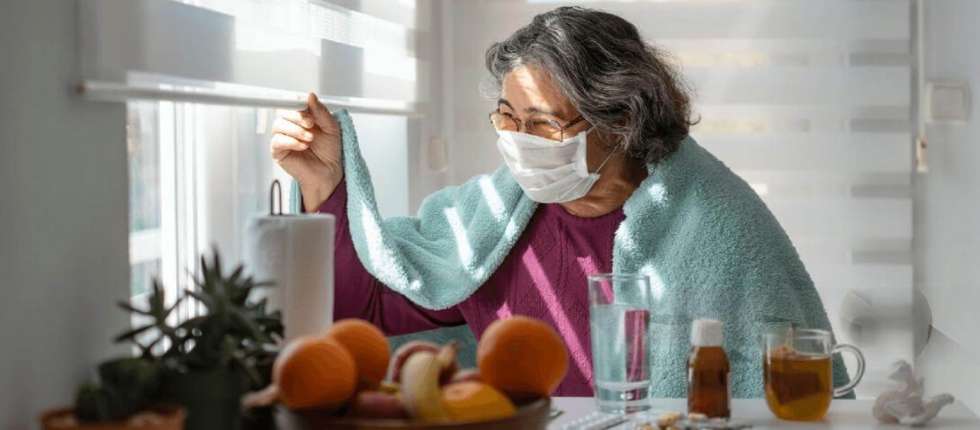 Mujer con COVID prolongado llevando una máscara, mirando por la ventana