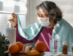 Mujer con COVID prolongado llevando una máscara, mirando por la ventana