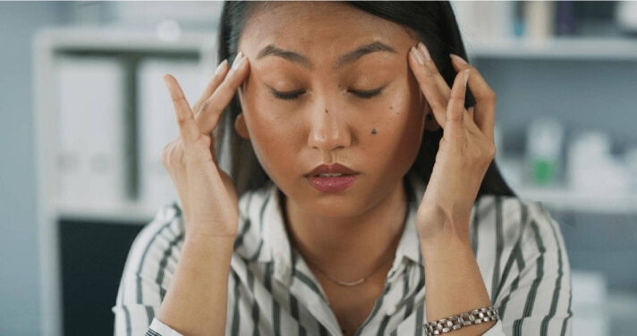 Mujer que experimenta síntomas prolongados de COVID, con los ojos cerrados y masajeándose la frente.